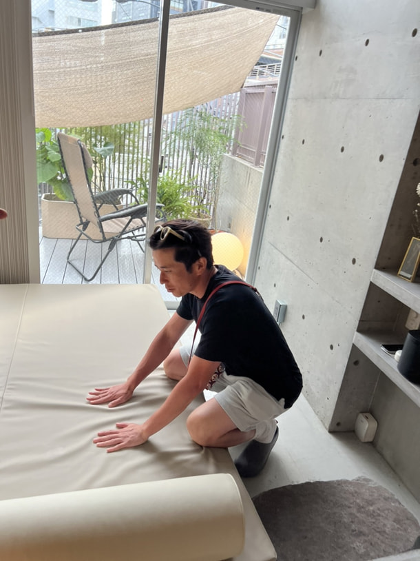 ARCH客室のベッドの感触を手で確かめる藤森慎吾さん。奥は外気浴のテラス