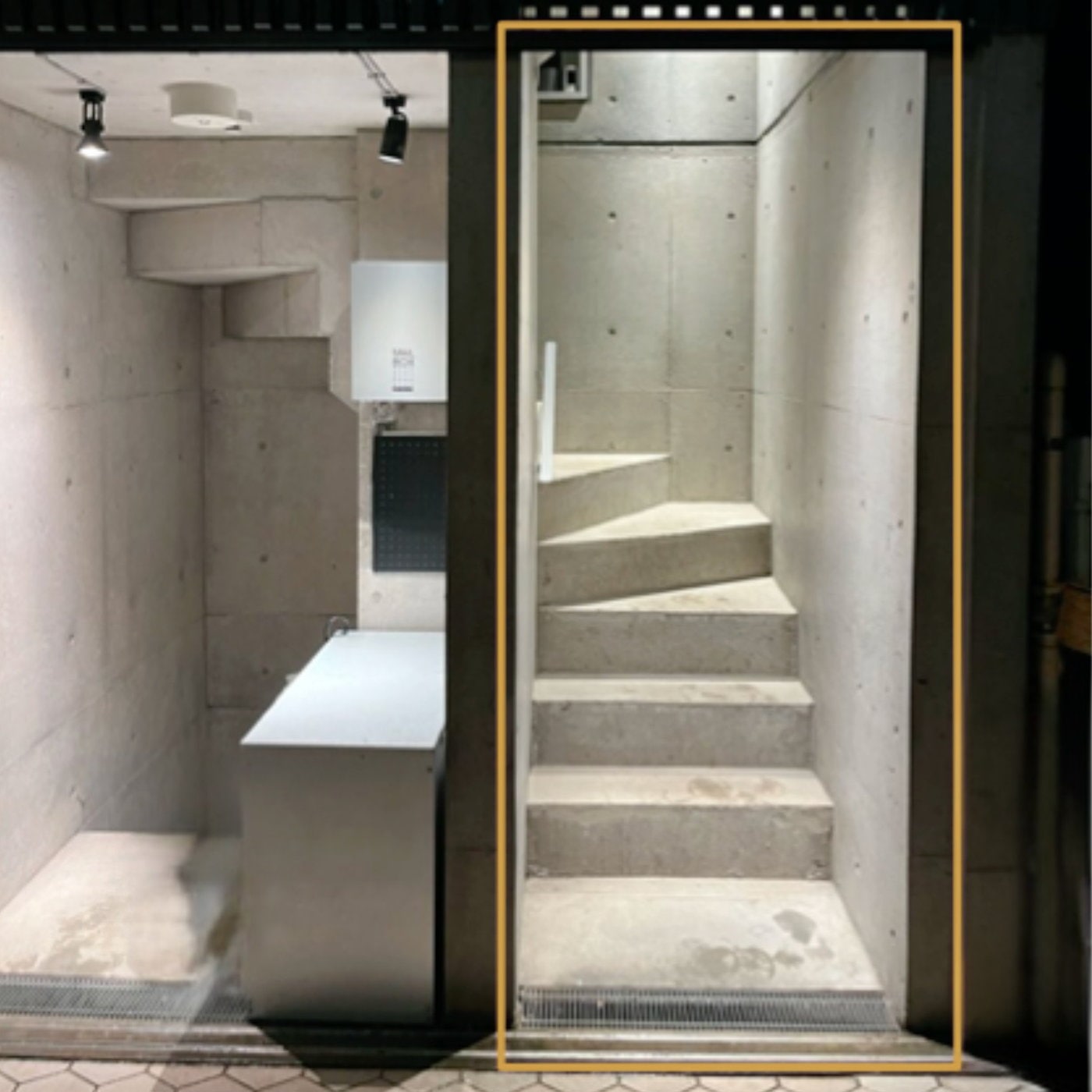 建物右手の通路を正面から見たところ。金色の枠で囲まれた開口部の奥に、上へ続くコンクリートの階段がある