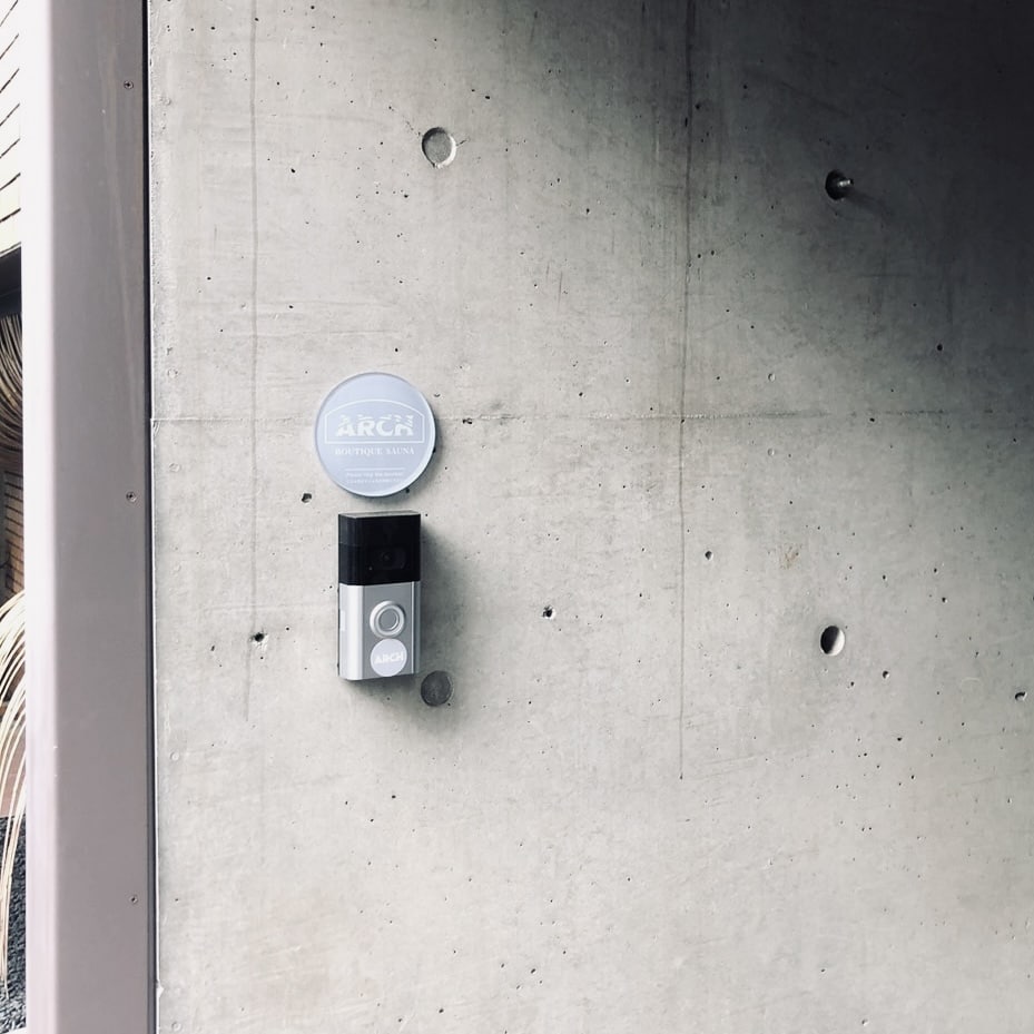 コンクリートの壁に取り付けられたARCHの丸いプレートと、その下のインターホン